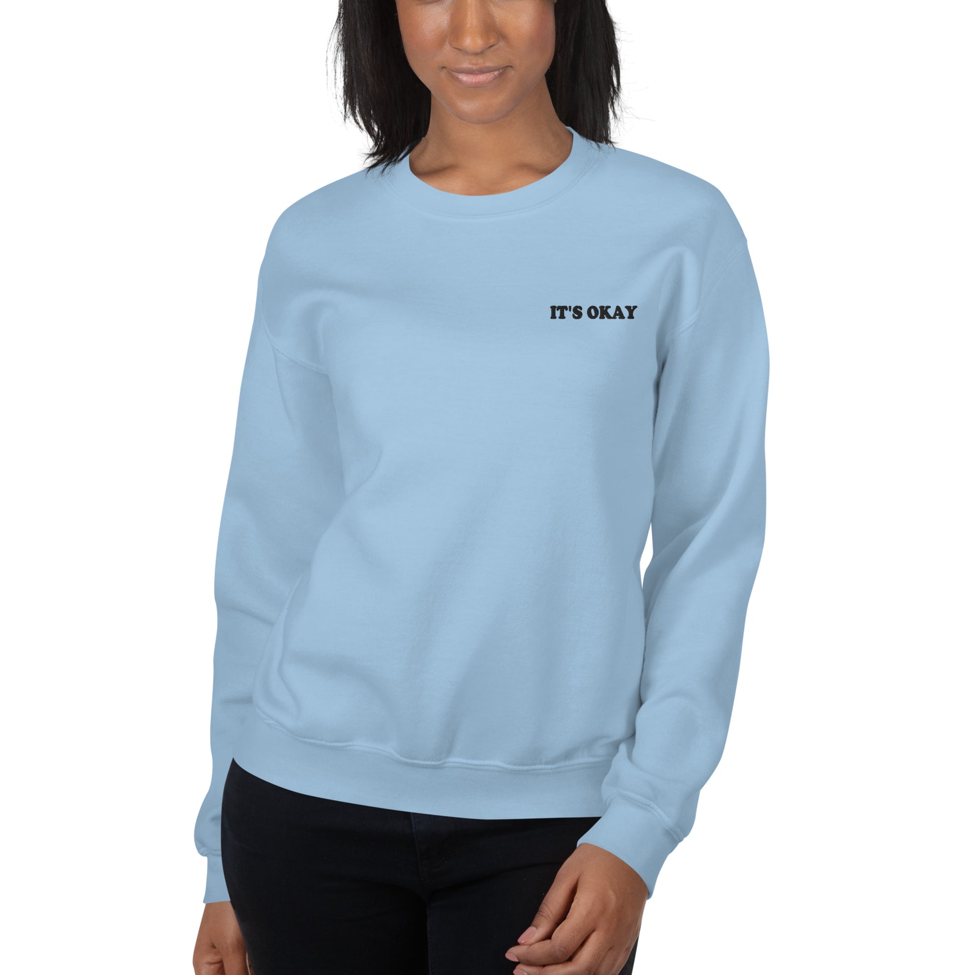 Light blue sweatshirt with 'IT'S OKAY' text worn by a person on a white background