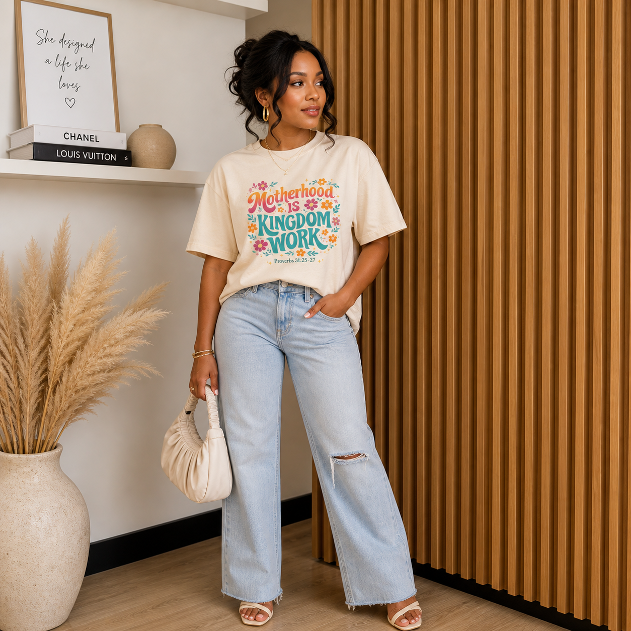 black woman posing wear an ivory shirt with colorful text that reads Motherhood Is Kingdom Work